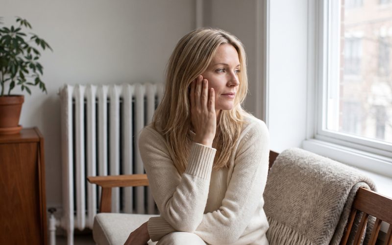 Woman sitting by a window next to a radiator in autumn light